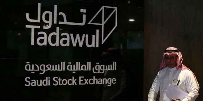 رجل يقف جوار لوحة السوق المالية السعودية