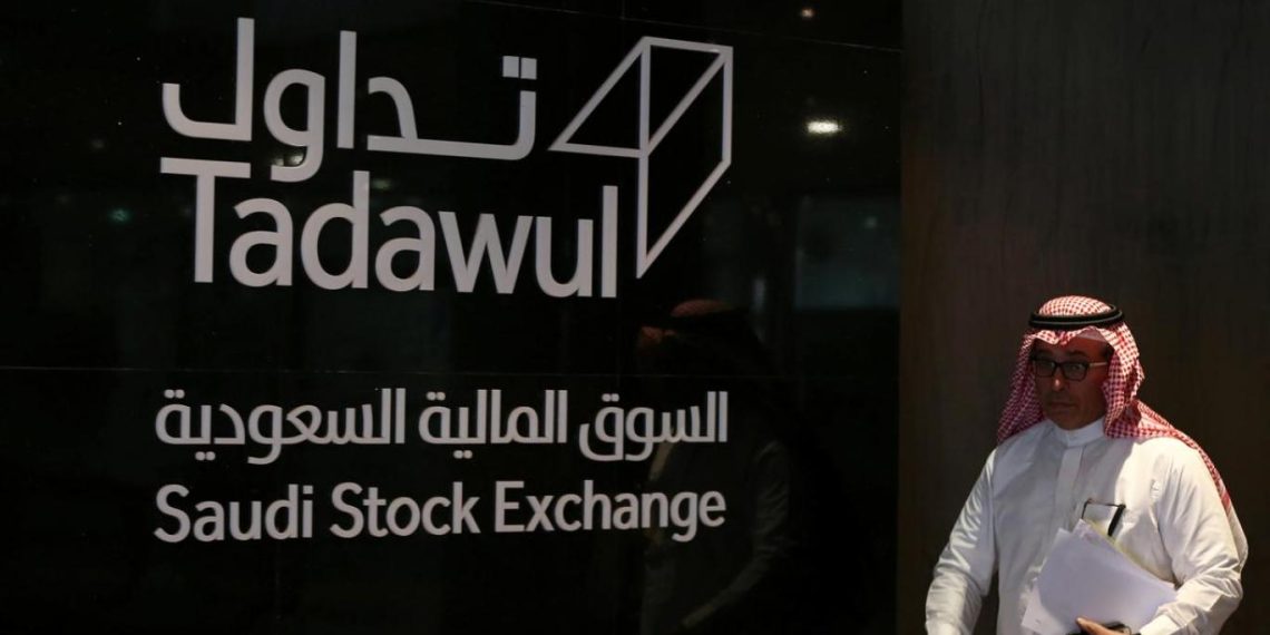 رجل يقف جوار لوحة السوق المالية السعودية